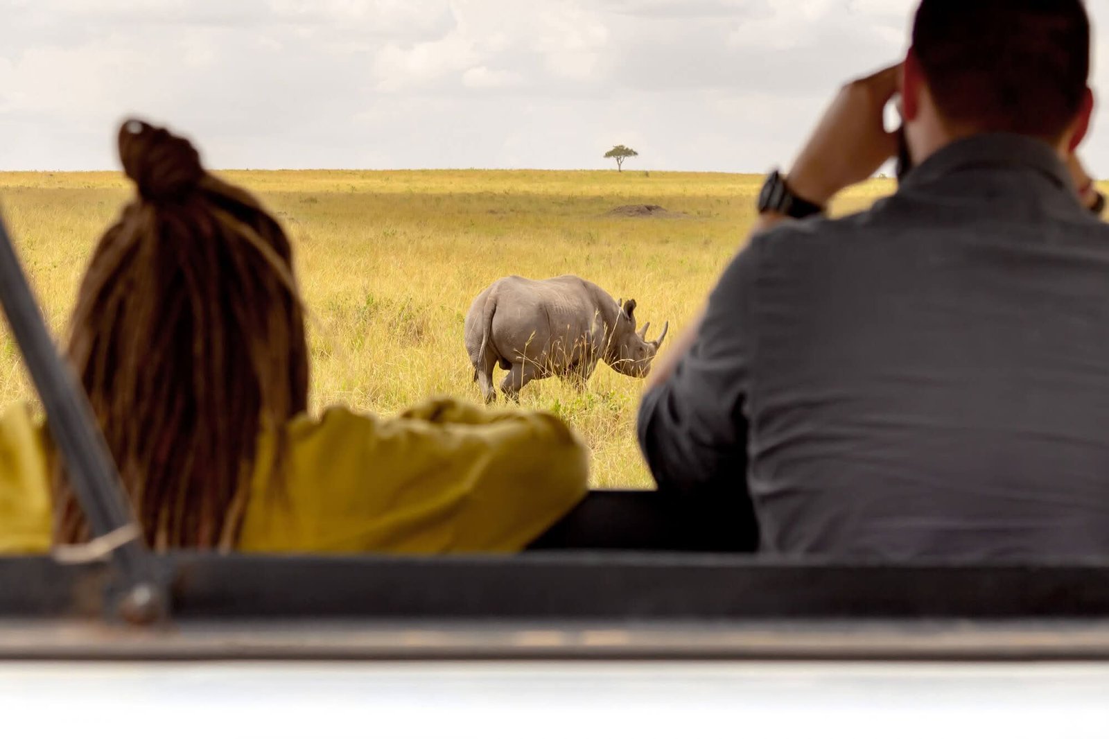 Couple on a Serengeti safari game drive watching a rhinoceros in Tanzania's vast grasslands.